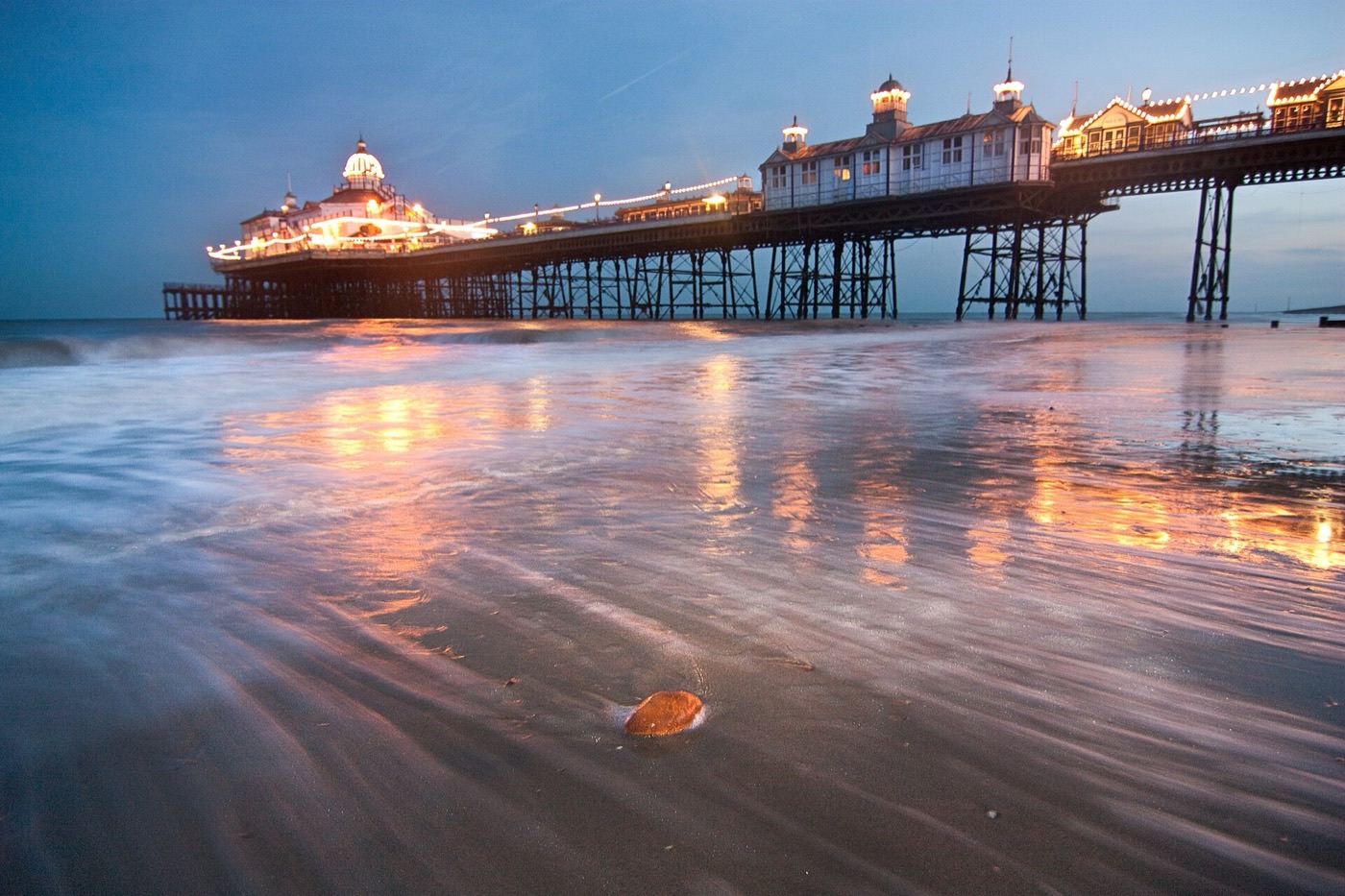 Eastbourne Pier at dusk, its lights reflected on the wet sand