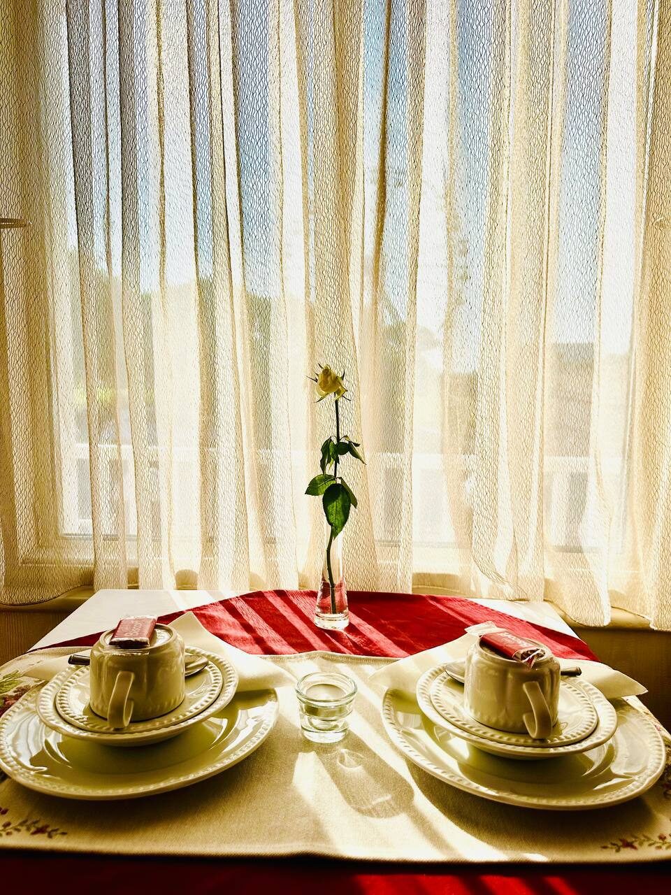 Breakfast table for two by the window with a single fresh rose