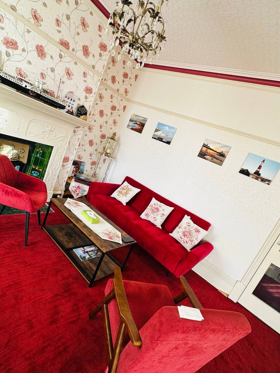 Our guest lounge — a red velvet sofa and original fireplace, framed by Eastbourne coastal prints